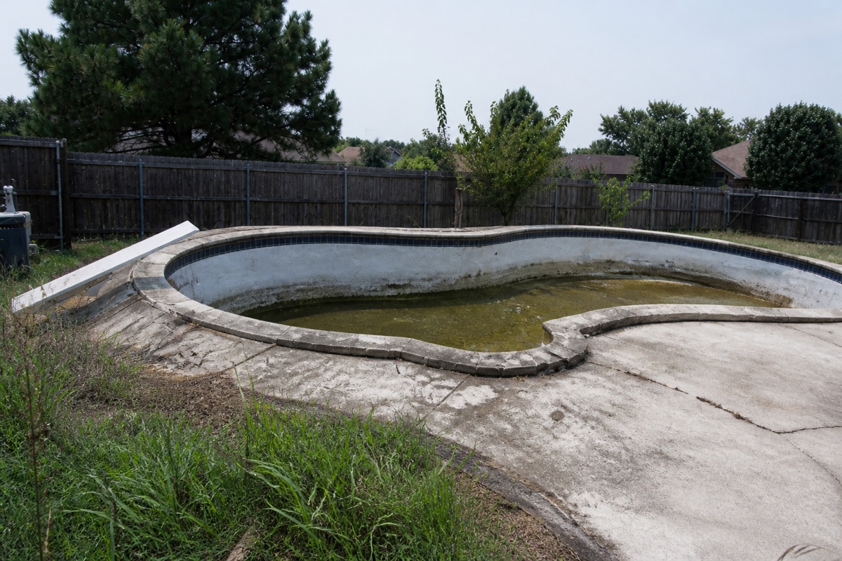 Empty freeform pool with cracked decking, the kind of existing vessel that decides retrofit options.