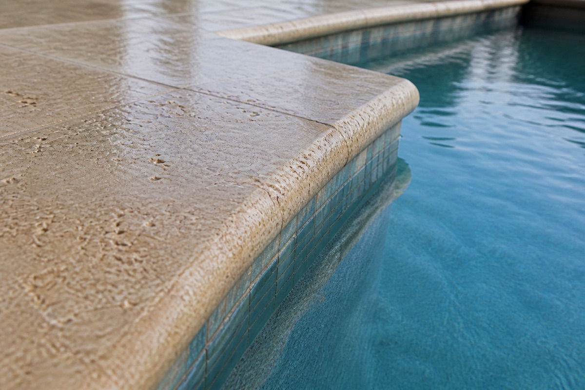 Close-up of stone pool coping meeting still blue water at the waterline.